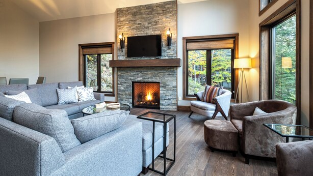 Una sala de estar moderna con chimenea de piedra, asientos cómodos y ventanas grandes que ofrecen vistas al exterior.