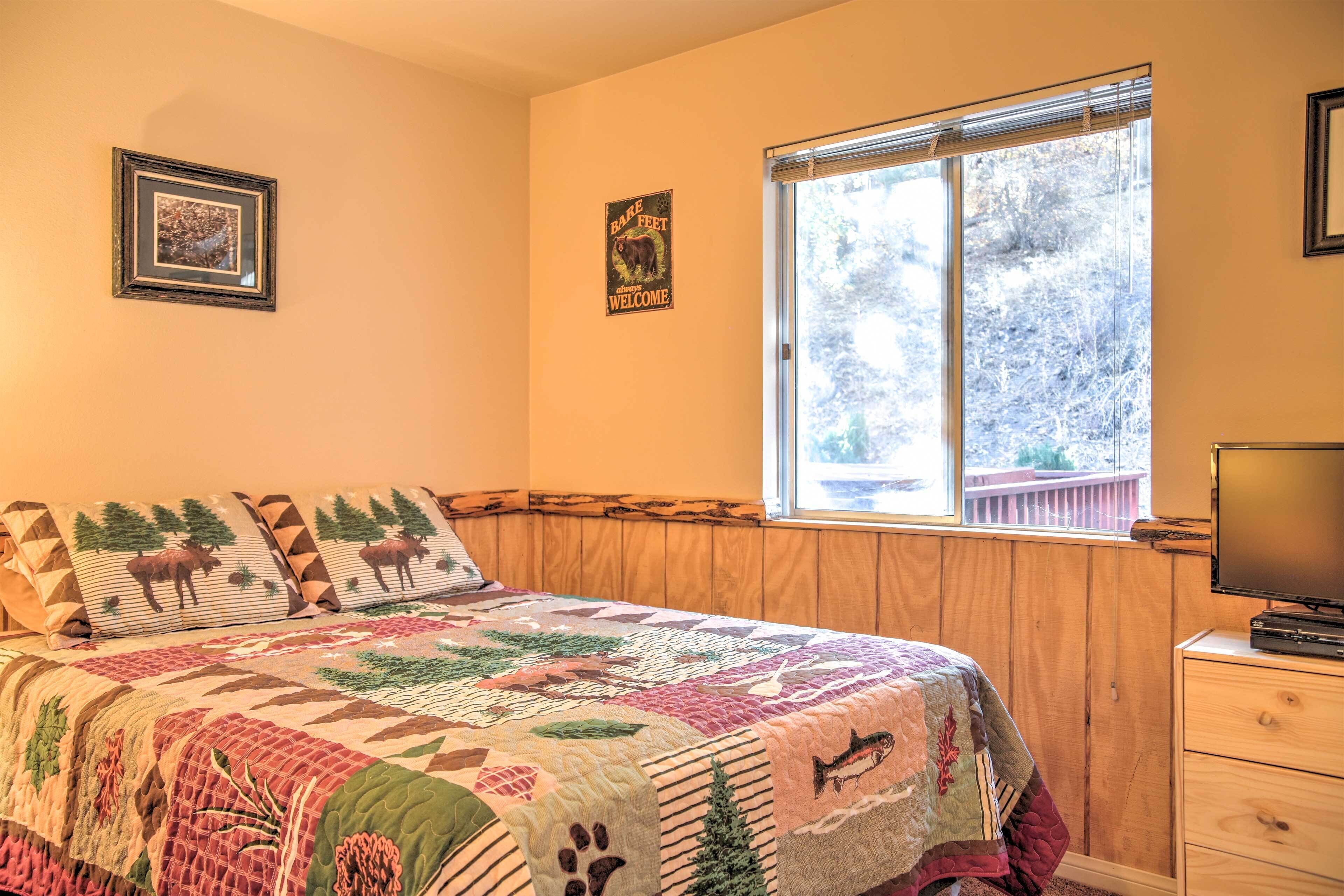 A bedroom with a large bed, a window with a view of trees, a wooden headboard, and a television on a dresser.
