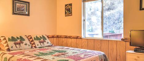 A bedroom with a large bed, a window with a view of trees, a wooden headboard, and a television on a dresser.