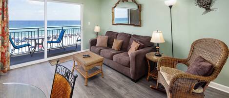 Sala de estar com varanda vista para a praia, mobiliada com sofá, cadeiras e mesa de jantar.