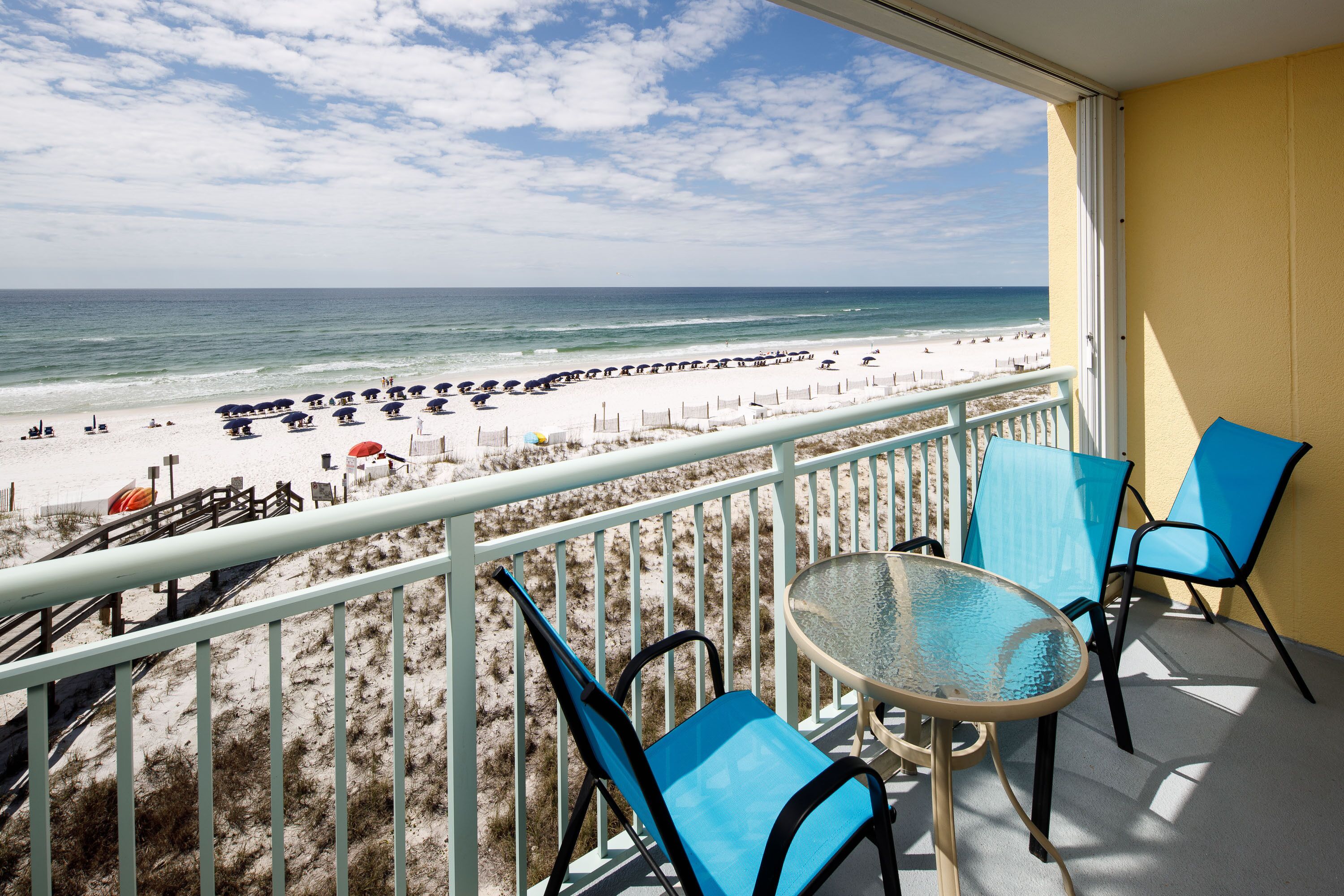A balcony with a view of a beach, equipped with a table and chairs.