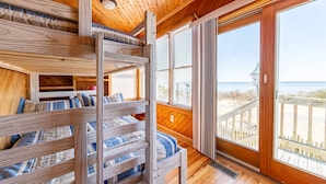 A wooden cabin with bunk beds, large windows, and a view of the beach. - Doggone Perfect - Village at Nags Head, Soundfront, Golf Course View, Pool, Hot Tub, Pets OK (Nags Head)