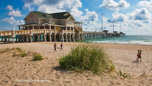 A beach house with a pier extending into the ocean, featuring a balcony and a view of the sea. - Doggone Perfect - Village at Nags Head, Soundfront, Golf Course View, Pool, Hot Tub, Pets OK (Nags Head)