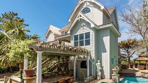 A large house with a swimming pool, outdoor seating, and a pergola. - Doggone Perfect - Village at Nags Head, Soundfront, Golf Course View, Pool, Hot Tub, Pets OK (Nags Head)