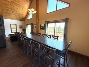 A spacious dining area with a long wooden table, multiple chairs, and a chandelier.