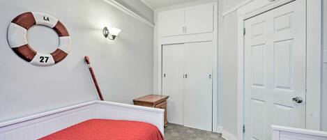 A bedroom with a bed, a nightstand, a dresser, a door, and a wall-mounted light fixture.