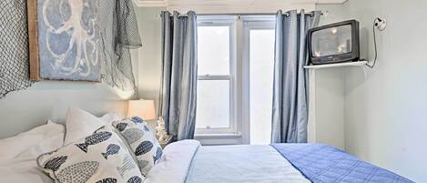 A bedroom with a bed, a television mounted on the wall, and a window with curtains.