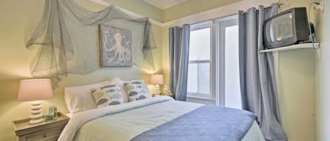 A bedroom with a bed, a nightstand, a television, and a window with curtains.