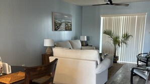 A living room with a sofa, a dining table with chairs, a ceiling fan, and a potted plant. - Ocean view! No drive Beach in New Smyrna Beach! (New Smyrna Beach)