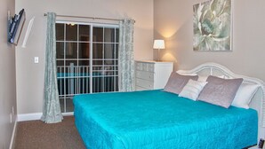 A bedroom with a bed, a dresser, a lamp, a ceiling fan, a window with curtains, and a painting on the wall. - Cherry Grove Villas 204, Golf Villa Bliss near Ocean (North Myrtle Beach)