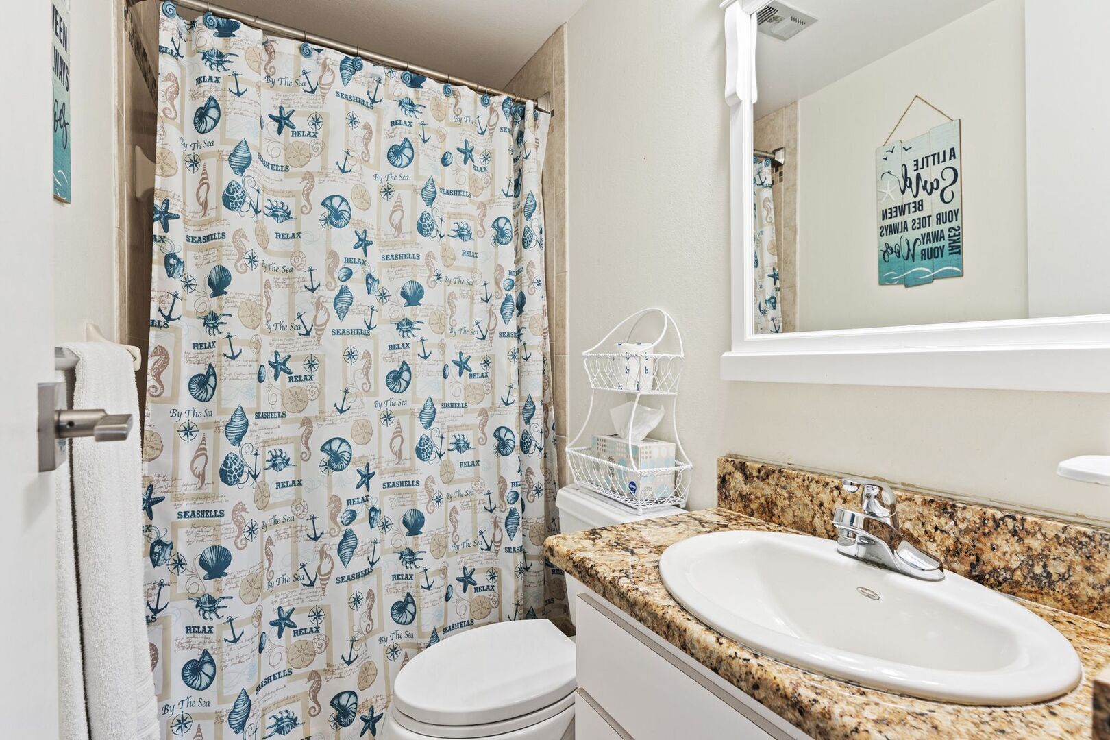 Kylpyhuone, jossa on meriaiheinen suihkuverho, graniittitasoinen pesuallas ja valkoinen wc-istuin.