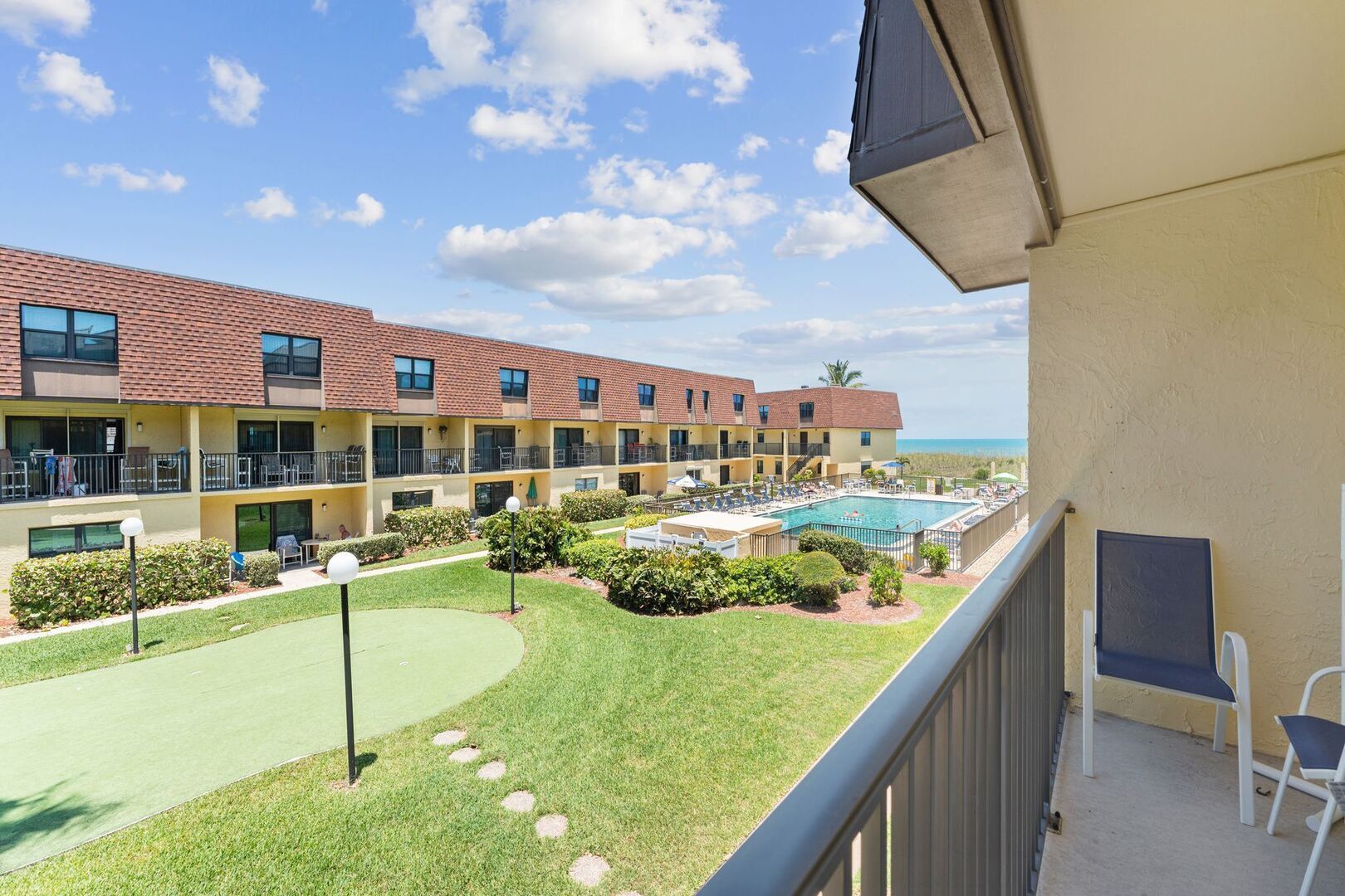 A hotel with multiple balconies, a swimming pool, and a well-maintained lawn.