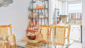 Un coin repas avec une table en verre, des chaises en osier et une étagère contenant des livres et des objets décoratifs.