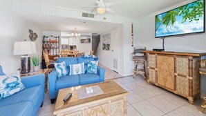 Un salon avec un canapé bleu, une table basse en bois et un téléviseur fixé au mur.