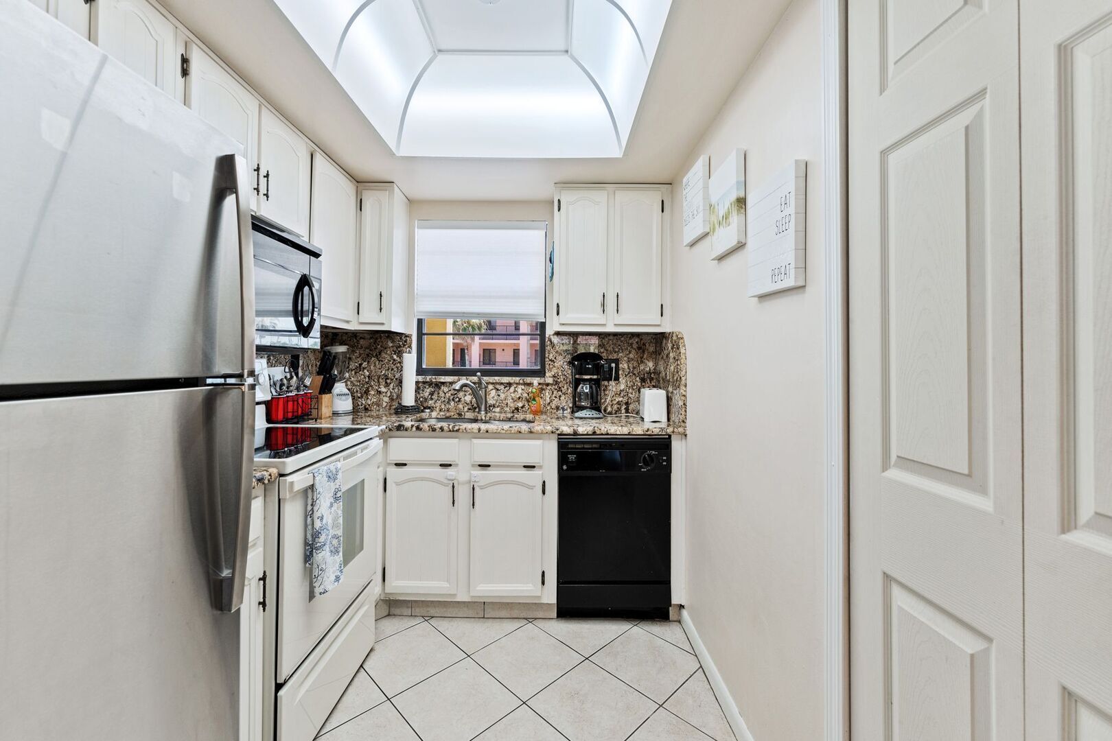 A narrow kitchen with white cabinets, a stainless steel refrigerator, a coffee maker, and a dishwasher.