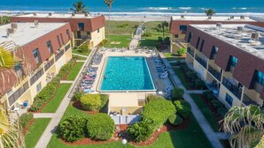 Une piscine sur le toit offrant une vue sur la plage, entourée d’immeubles dotés de balcons et d’un jardin bien entretenu.