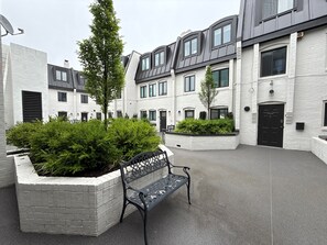 A courtyard with a bench, white brick buildings, and greenery.