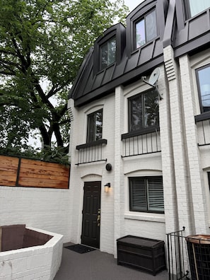 A two-story building with a white brick facade, a dark brown door, and a small front porch.