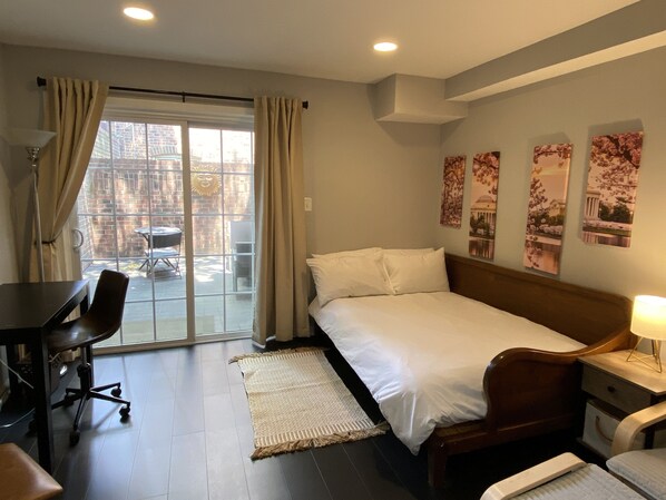 A hotel room with a bed, desk, chair, and a view of the outside through a glass door.
