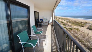 Een balkon met uitzicht op het strand, met een tafel en stoelen.
