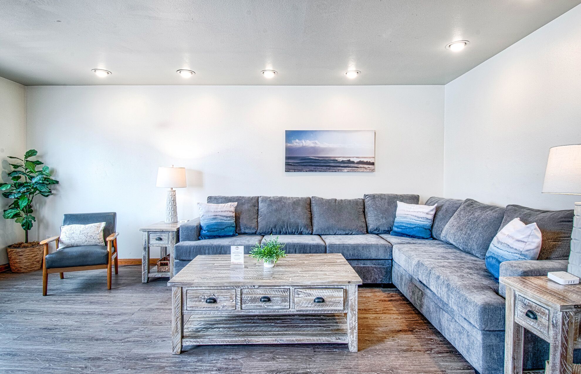 A modern living room with a grey sectional sofa, a wooden coffee table with drawers, a potted plant, and a wall-mounted picture.