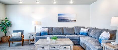 A modern living room with a grey sectional sofa, a wooden coffee table with drawers, a potted plant, and a wall-mounted picture.
