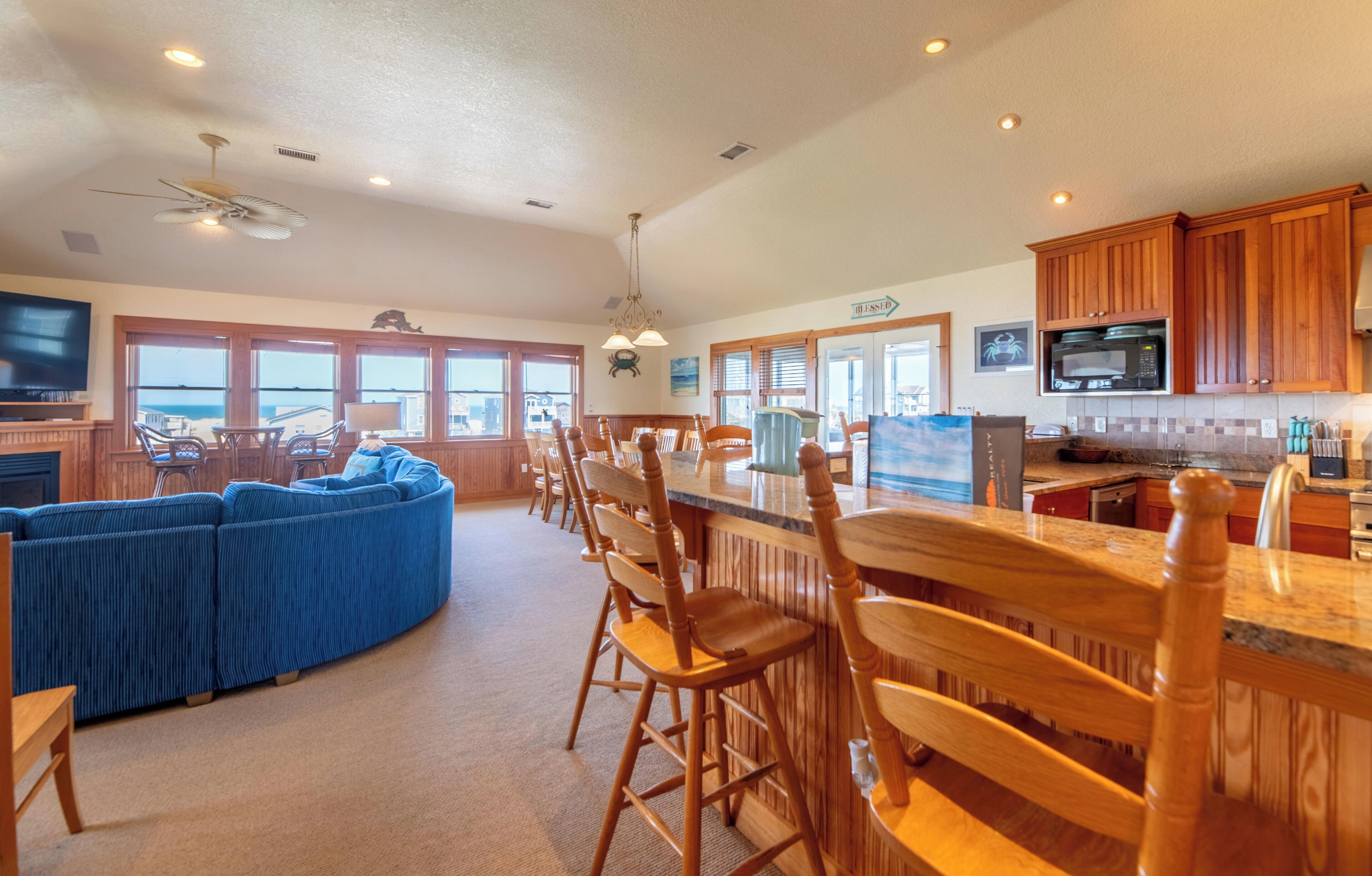 Une cuisine spacieuse avec des meubles en bois, un coin bar et un espace salon agrémenté d’un canapé bleu.