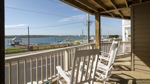 A wooden deck with white chairs overlooking a waterfront area with a pier and a view of a bridge. - Comfortable sound-front duplex near Crystal Pier! (Wrightsville Beach)