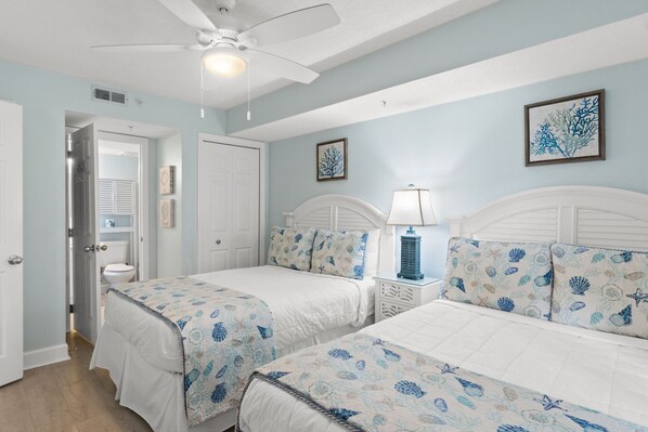 A bedroom with two beds, a ceiling fan, and a nightstand with a lamp.