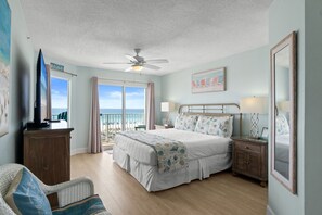 Un dormitorio con una cama grande, un ventilador de techo, vista a la playa y una obra de arte con temática playera en la pared.