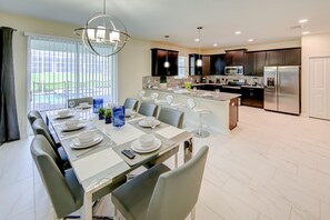 A modern kitchen with dark cabinets, stainless steel appliances, and a dining area with a table set for six. - ChampionsGate Villa Walk to Oasis Clubhouse Private Pool GolfResort Amenities (Davenport)