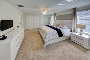 A bedroom with a bed, a TV, a ceiling fan, a dresser, and a window with curtains.