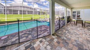 Un patio couvert avec une piscine, des sièges d’extérieur et une vue sur un quartier résidentiel.