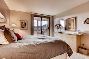 A bedroom with a bed, a dresser, a mirror, and a window with a mountain view.