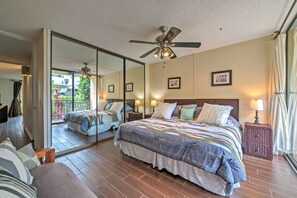 Um quarto com um espelho grande, um ventilador de teto, uma cama com um edredom colorido e uma mesa de cabeceira com abajur.