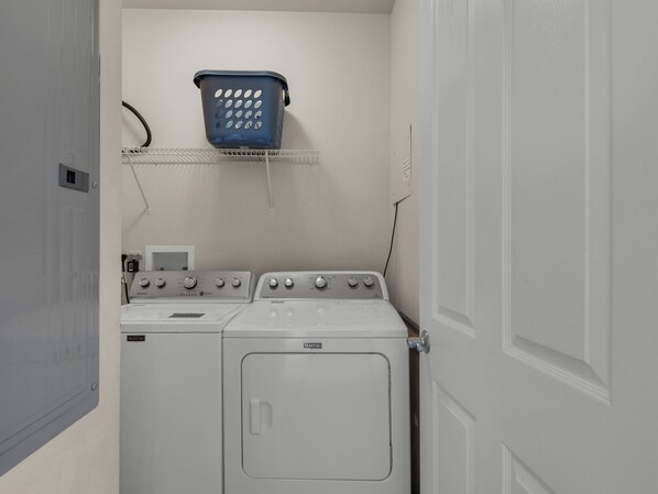 Un'area lavanderia con lavatrice e asciugatrice Maytag, uno scaffale in metallo e un cesto per la biancheria blu.