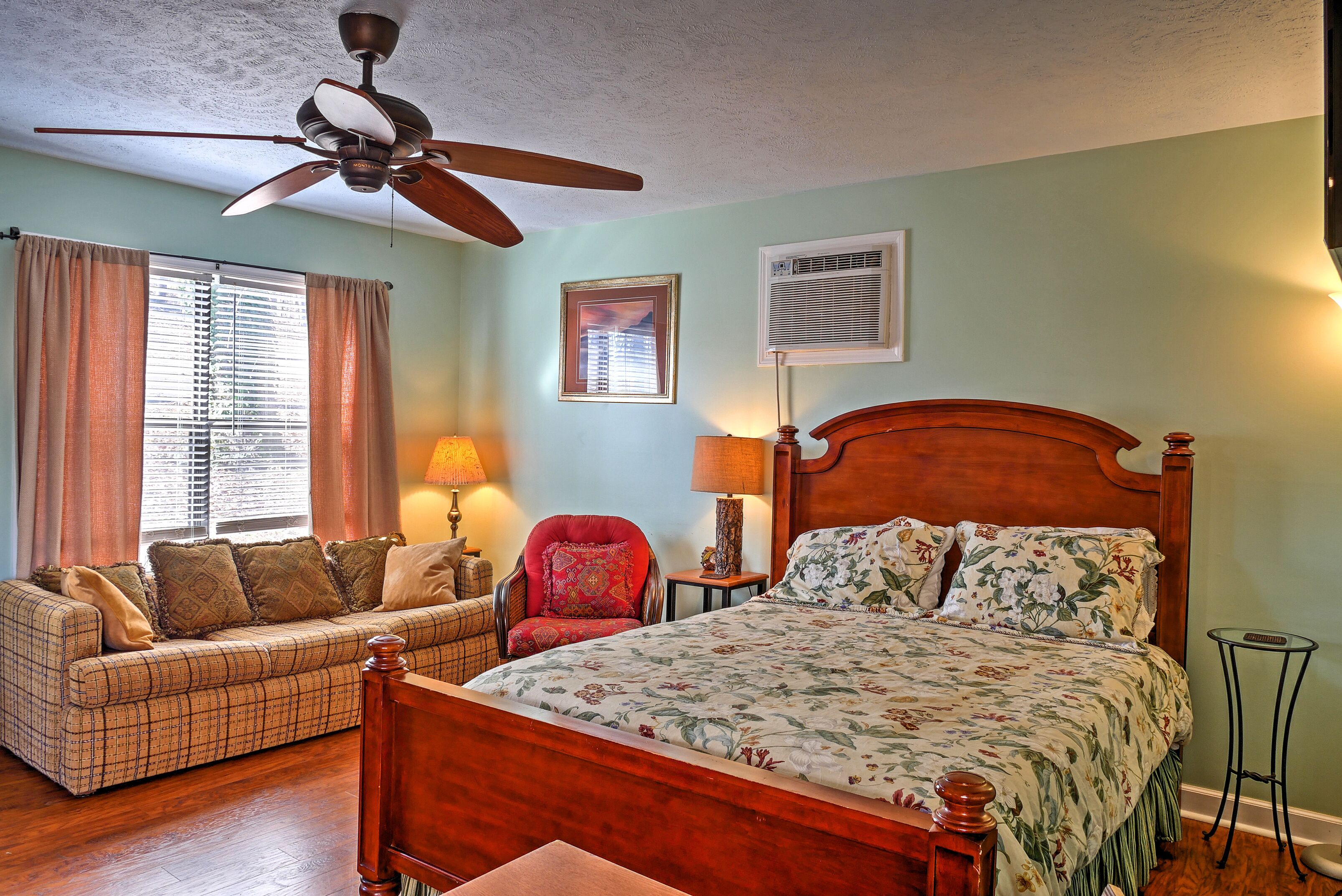 A bedroom with a wooden bed, a sofa, a red armchair, and a ceiling fan.