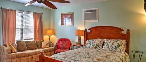 A bedroom with a wooden bed, a sofa, a red armchair, and a ceiling fan.