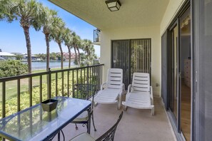 Enjoy a serene view of the water and palm trees from this balcony, featuring two lounge chairs and a table.