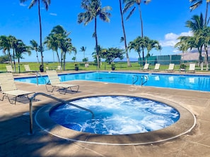 A swimming pool with lounge chairs, a hot tub, palm trees, and a clear sky.