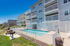 Enjoy a refreshing swim in the pool surrounded by a white fence, with lounge chairs and a barbecue grill nearby.