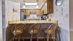 A kitchen with wooden cabinets, a granite countertop, and three wicker chairs. - *Fall into Savings-20% Off New Bookings thru 2026* (Surfside Beach)