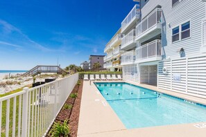 A pool area with a wooden deck and a view of the beach.