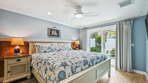 Ein Schlafzimmer mit einem Bett, zwei Nachttischen, einem Deckenventilator und einem Fenster mit Vorhängen.
