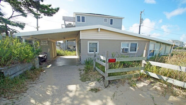 A two-story house with a covered porch, a sandy driveway, and a wooden fence. - SN9017D- Semi-OF!  With 3 BRs, Direct Beach Access, Private and Secluded! (Nags Head)