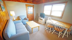 A cozy living room with a sofa, a coffee table, a TV on a stand, and a dining table with chairs. - SN9017D- Semi-OF!  With 3 BRs, Direct Beach Access, Private and Secluded! (Nags Head)