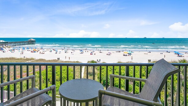Un balcon donnant sur une plage, avec des parasols et des gens.