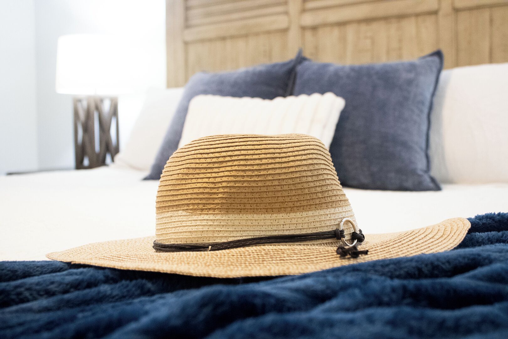 A straw hat with a black band on a bed with a dark blue blanket.