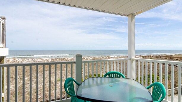 A covered outdoor area with a table and chairs, overlooking a beach with the ocean in the background.