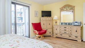 A bedroom with a bed, a red chair, a wooden dresser, a television, and a mirror.